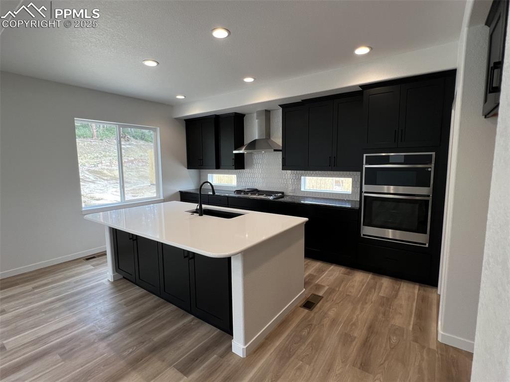 Image 4 of 17: Kitchen featuring dark cabinetry, recessed lighting, wall chimney exhaust h
