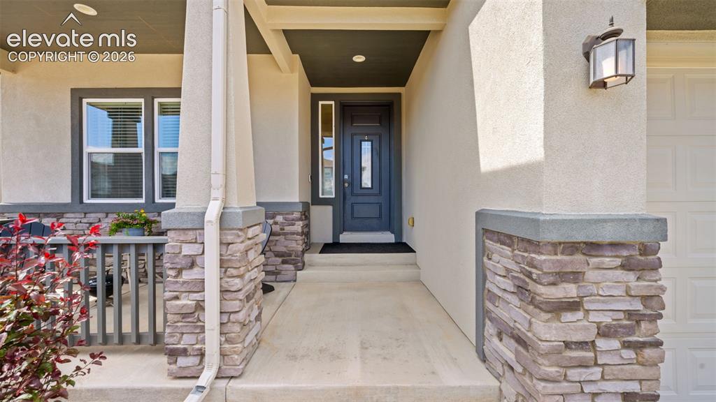 Image 4 of 39: Inviting covered entry with a contemporary dark gray door, stone-clad colum