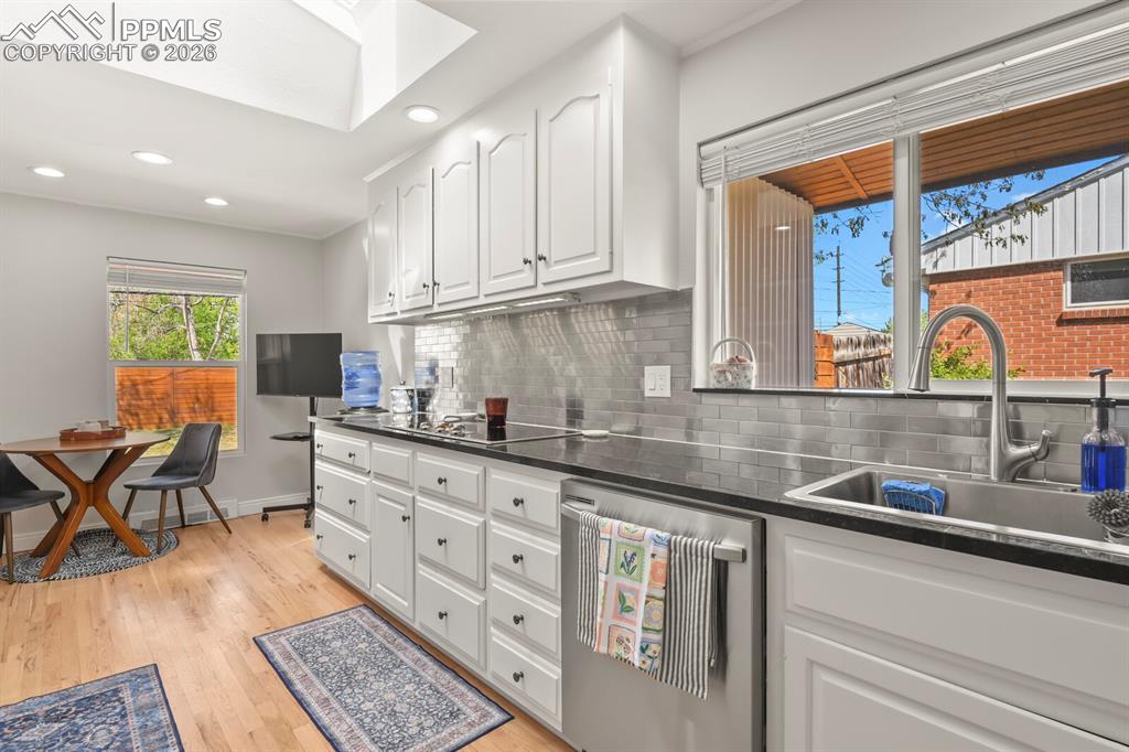 Image 11 of 48: Kitchen featuring white cabinetry, hardwood floors, stainless subway tile b