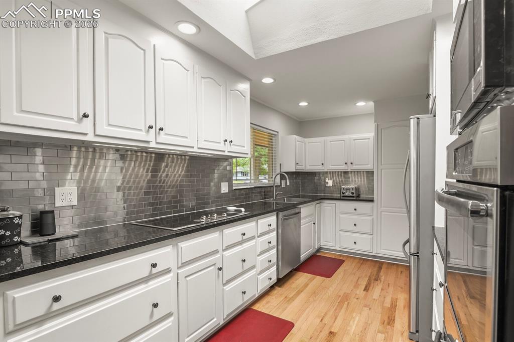 Image 8 of 48: Kitchen featuring white cabinetry, dark stone countertops, stainless steel