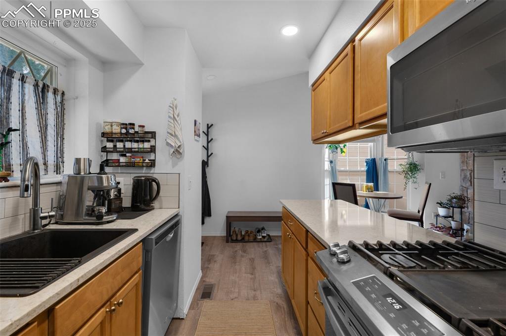 Image 14 of 26: Kitchen with appliances with stainless steel finishes, brown cabinetry, lig