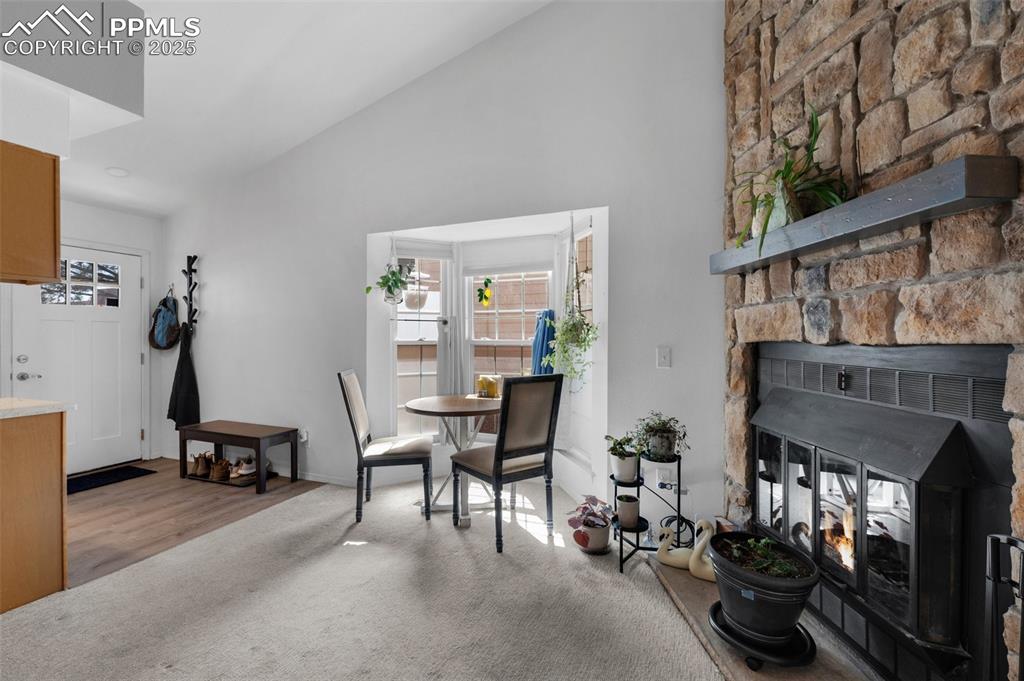 Image 7 of 26: Carpeted dining area featuring a wood-burning fireplace and high vaulted ce
