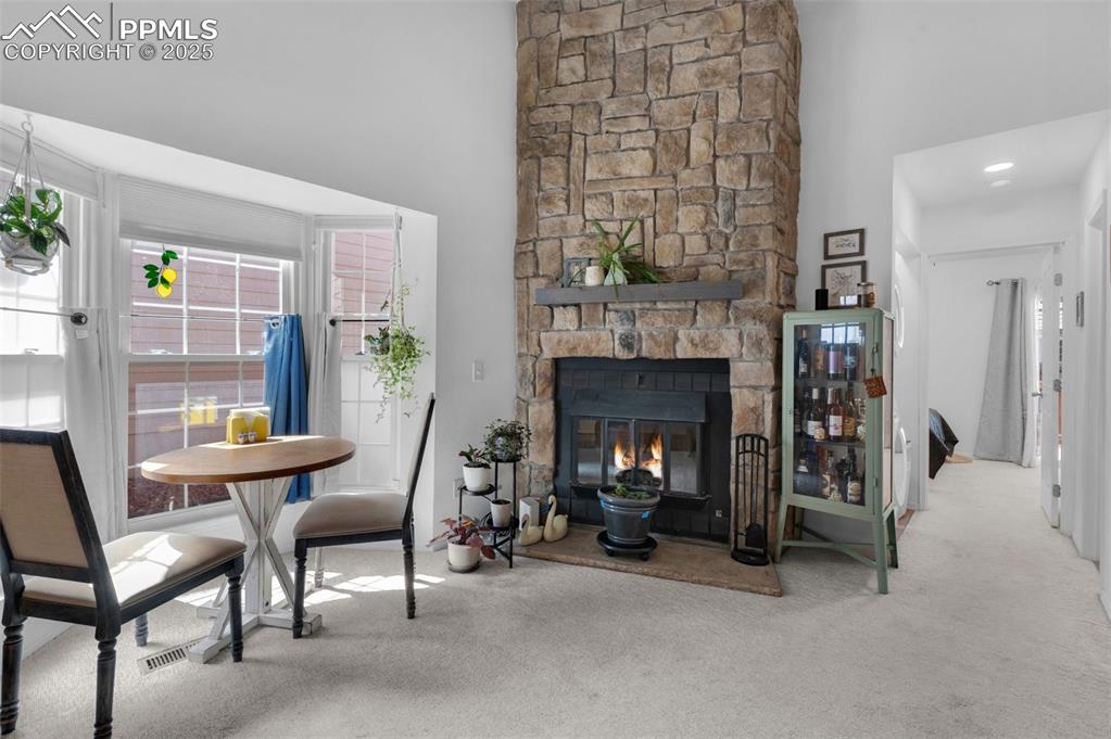 Image 8 of 26: Living area with a stone fireplace, carpet, and a high ceiling