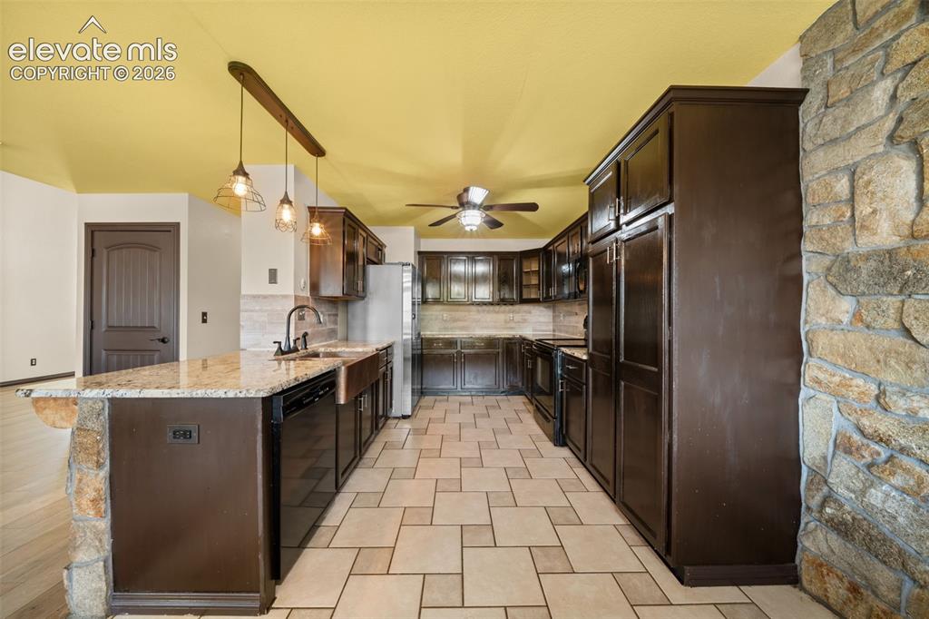 Image 15 of 49: Kitchen featuring extensive dark-finish cabinetry, light stone countertops,