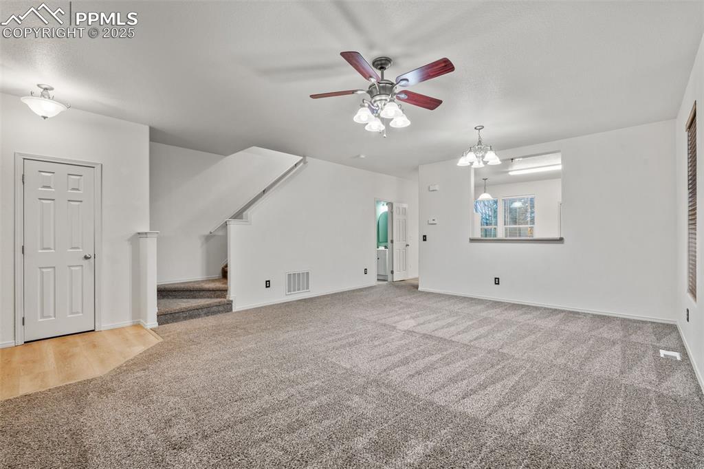 Image 6 of 20: Unfurnished living room with carpet, stairs, ceiling fan, and a chandelier