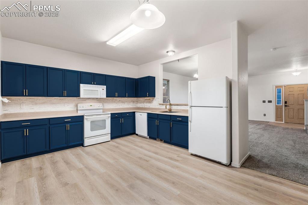 Image 8 of 20: Kitchen with white appliances, light countertops, blue cabinets, tasteful b