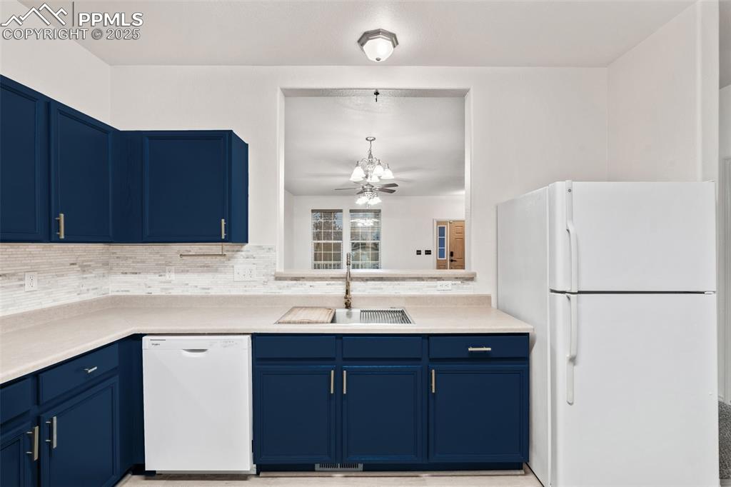Image 9 of 20: Kitchen with blue cabinets, white appliances, light countertops, and tastef