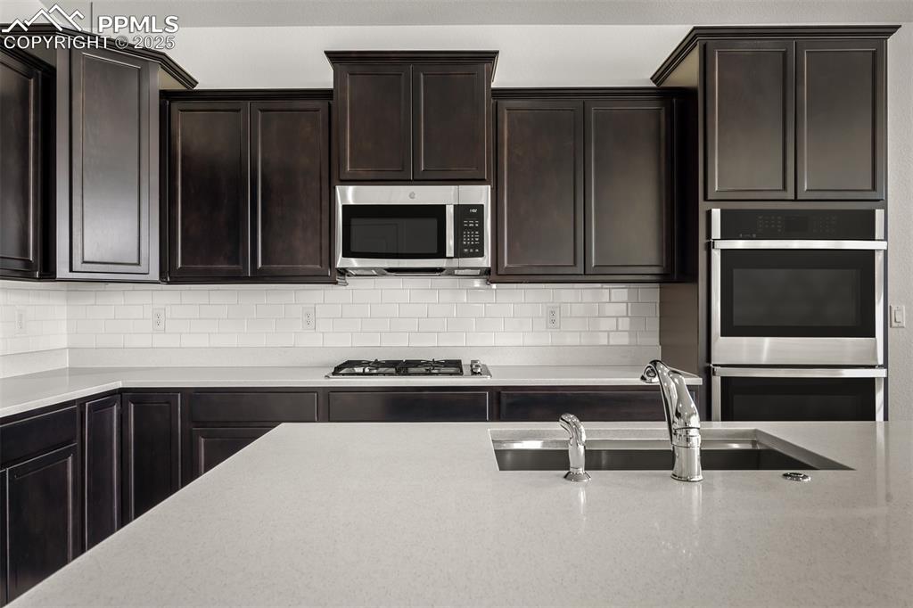 Image 15 of 46: Kitchen with stainless steel appliances, tasteful backsplash, dark brown ca