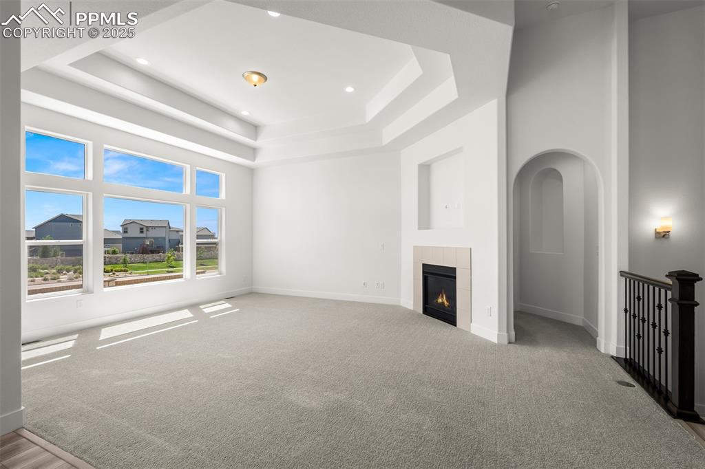 Image 22 of 46: Unfurnished living room with a high ceiling, a tray ceiling, carpet floorin