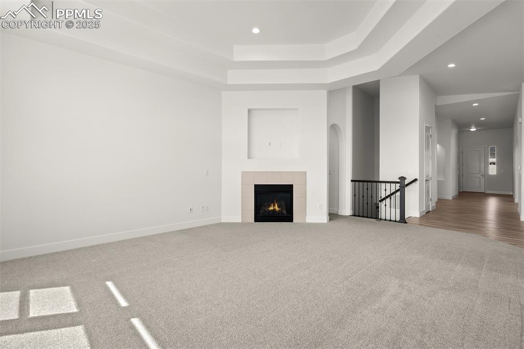 Image 23 of 46: Unfurnished living room featuring a raised ceiling, carpet flooring, recess