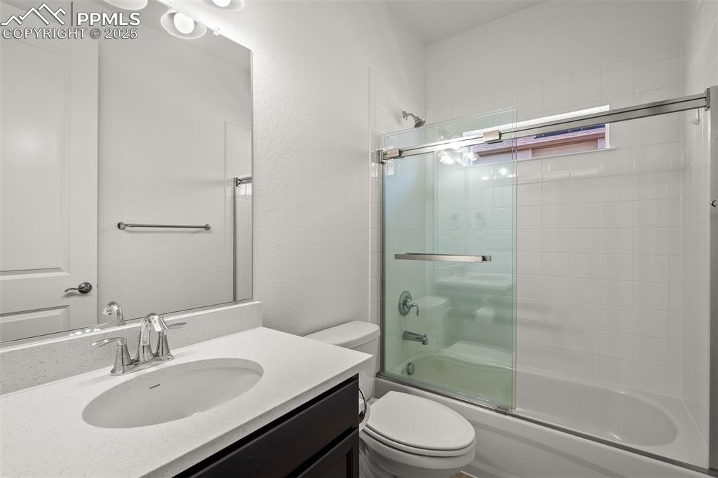 Image 36 of 46: Full bath featuring enclosed tub / shower combo, vanity, and a textured wal