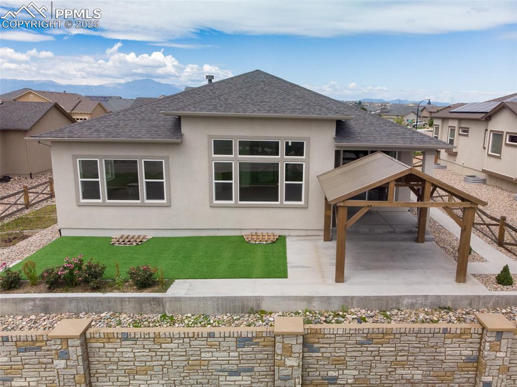 Image 6 of 46: Rear view of house featuring a shingled roof, stucco siding, and a mountain