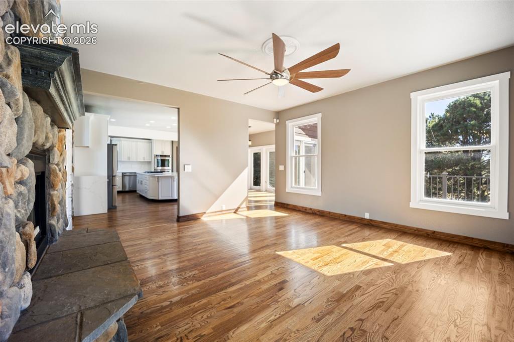 Image 14 of 40: Spacious living area featuring a stone fireplace with a stone hearth, wood-