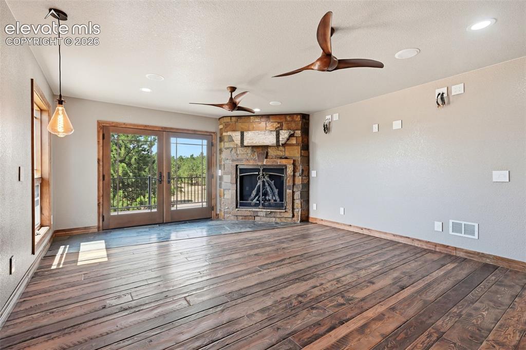 Image 16 of 40: Spacious room featuring wood-finish flooring, a corner stone fireplace, and