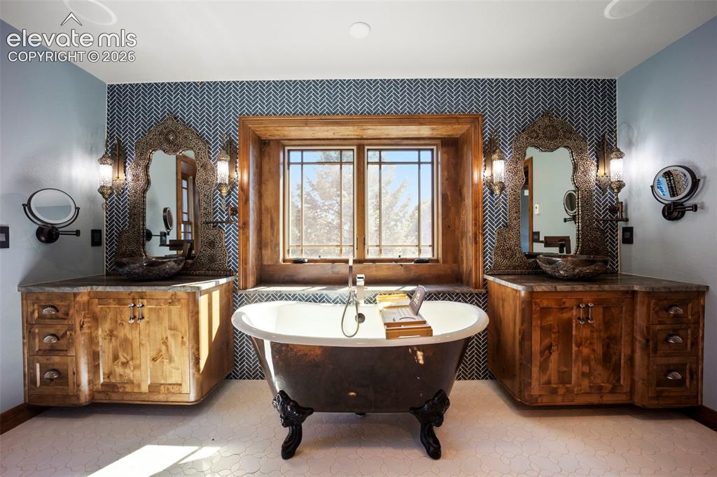 Image 19 of 40: Freestanding bathtub with claw feet, flanked by two rustic wood vanities wi