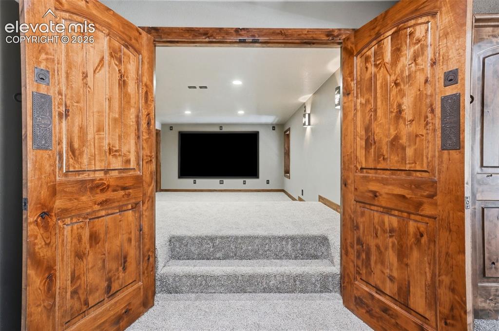 Image 26 of 40: Double wood doors with dark hardware open to a carpeted room featuring a la