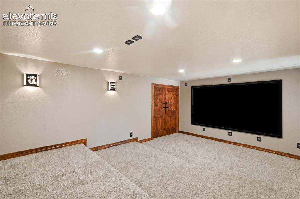 Image 27 of 40: Dedicated media room featuring a large projection screen, tiered carpeting,