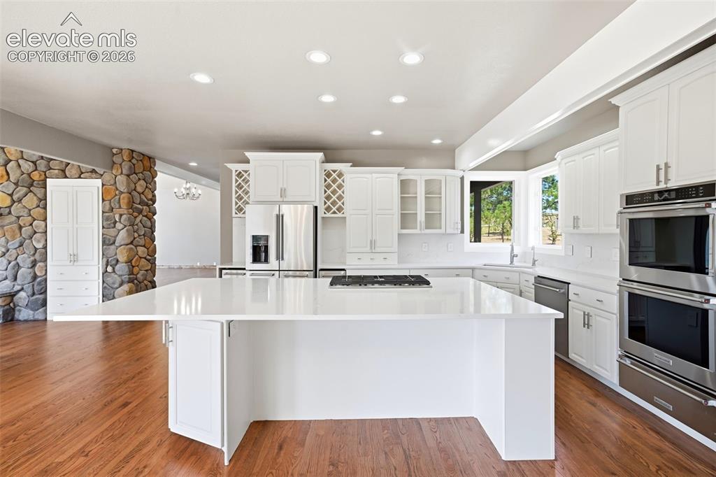 Image 6 of 40: Contemporary kitchen featuring a large central island with a cooktop, white