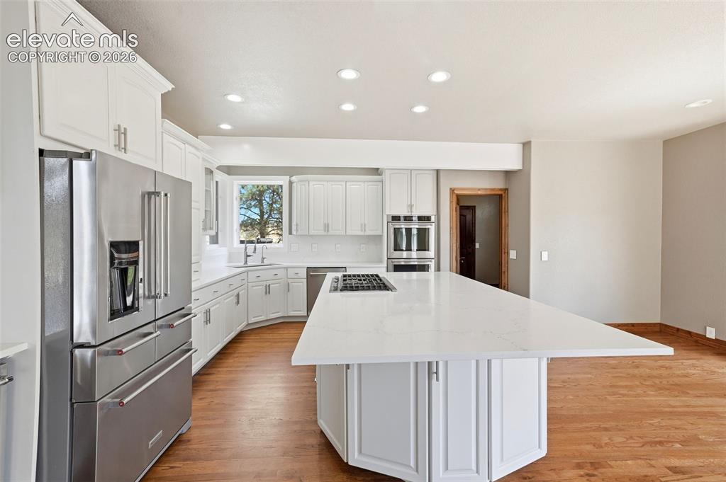 Image 8 of 40: Modern kitchen featuring a large central island with a cooktop, white cabin