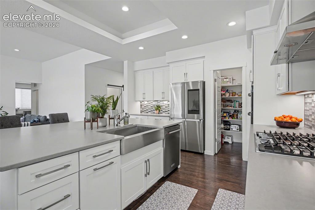 Image 12 of 41: Kitchen featuring white cabinets, stainless steel gas cooktop, suspended li
