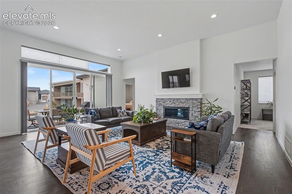 Image 6 of 41: Living room with dark wood finished floors, a stone fireplace, and recessed