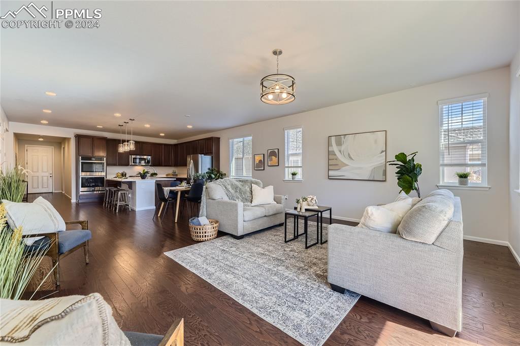 Image 7 of 50: Living room with dark wood-type flooring and an inviting chandelier