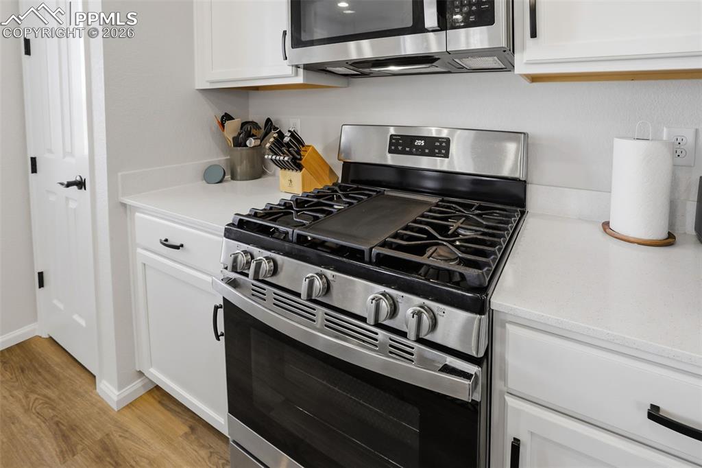 Image 5 of 28: Kitchen featuring stainless steel appliances, white cabinetry, light wood-t
