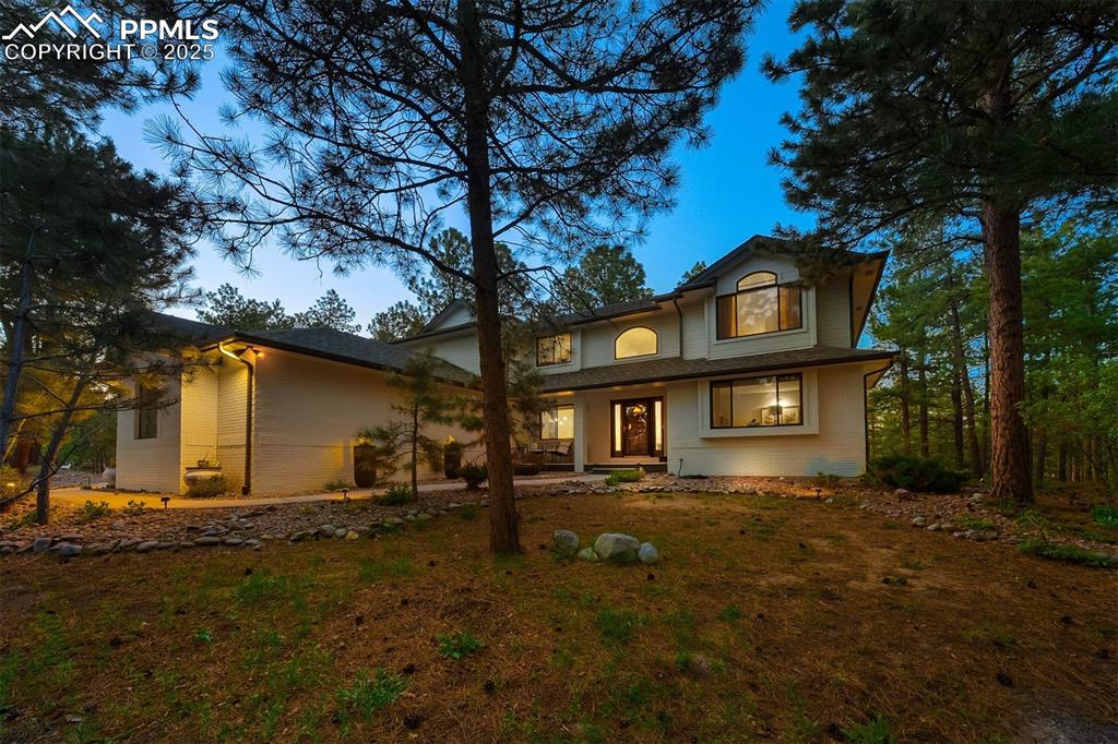 Image 27 of 30: Twilight view of the front of the home with towering pines.