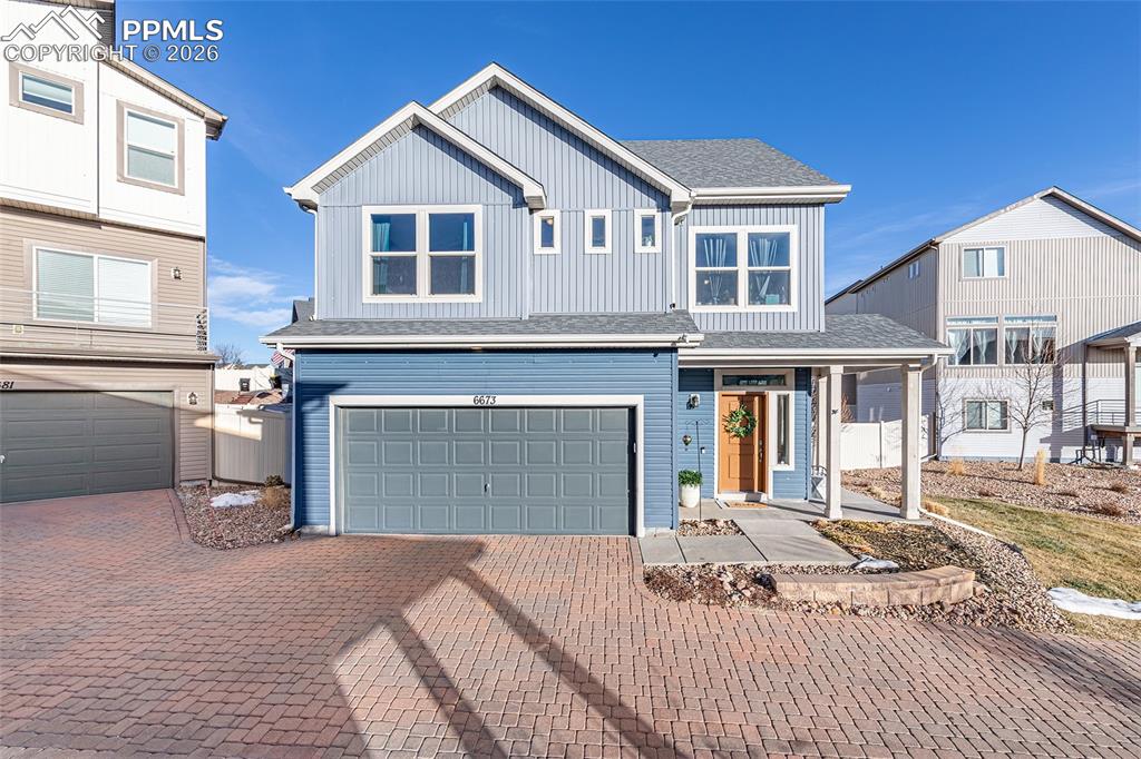 Caption: View of front facade featuring roof with shingles, an attached garage, decorative driveway, and a po