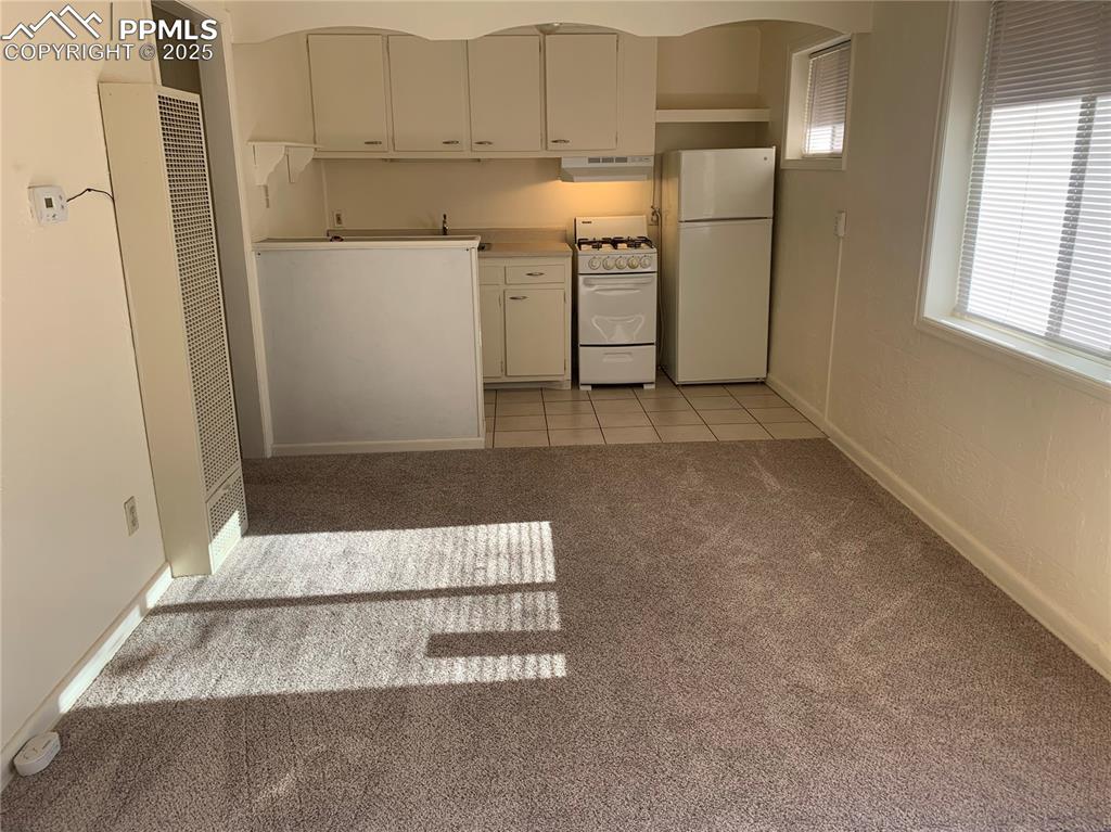 Image 6 of 11: Kitchen with white appliances, light colored carpet, a heating unit, light