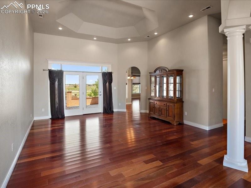 Image 10 of 48: Unfurnished living room featuring a tray ceiling, ornate columns, dark wood