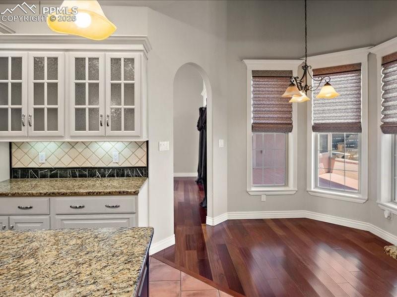 Image 28 of 48: Unfurnished dining area with arched walkways, dark wood-type flooring, and