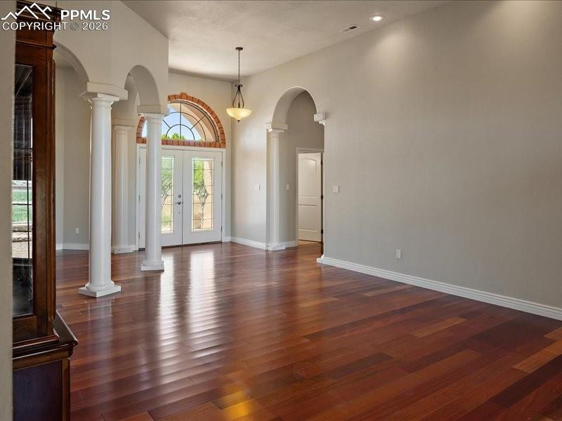 Image 42 of 48: Entrance foyer with decorative columns, dark wood finished floors, and a hi