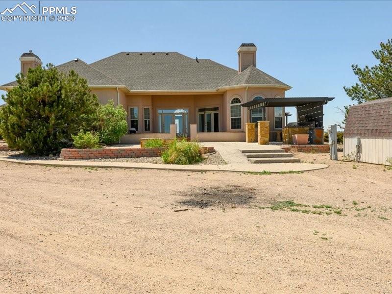 Image 43 of 48: Back of house featuring a chimney, a patio, roof with shingles, and stucco