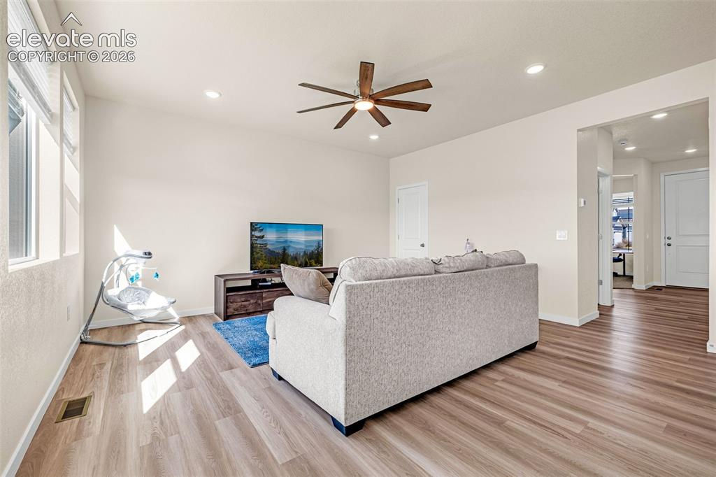 Image 10 of 50: Warm wood-finish flooring, recessed lighting, and a ceiling fan with wood-l