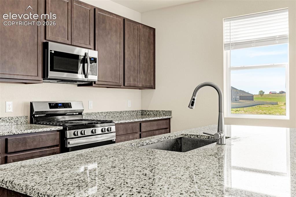 Image 11 of 50: Granite countertops, dark wood-finish cabinetry, stainless steel appliances