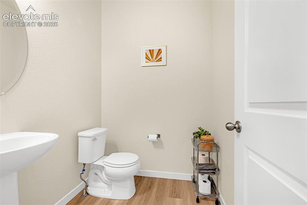 Image 33 of 50: Pedestal sink with an oval mirror, light-colored walls, wood-finish floorin