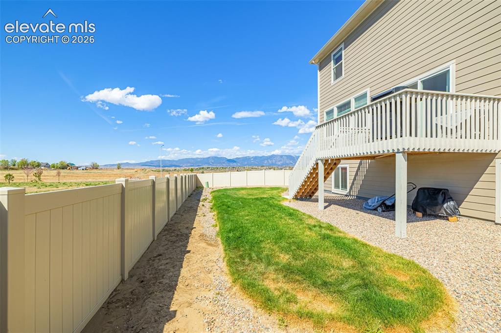 Image 41 of 50: Expansive backyard with a manicured lawn, gravel landscaping, and a tan pri
