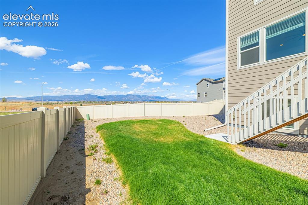 Image 42 of 50: Fenced backyard with a grassy lawn, gravel landscaping, and mountain scener