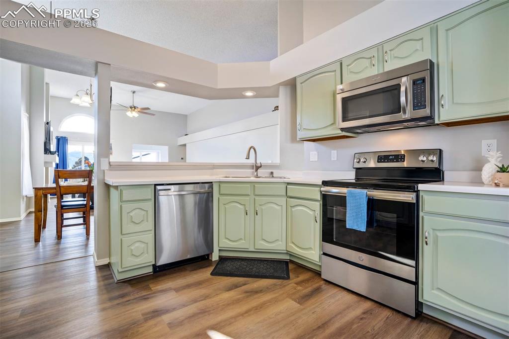Image 16 of 43: Kitchen featuring green cabinetry, stainless steel appliances, light counte