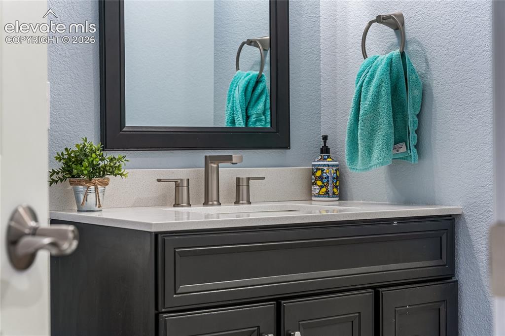 Image 24 of 32: Dual vanity with white cabinetry, dark countertop, and integrated sinks