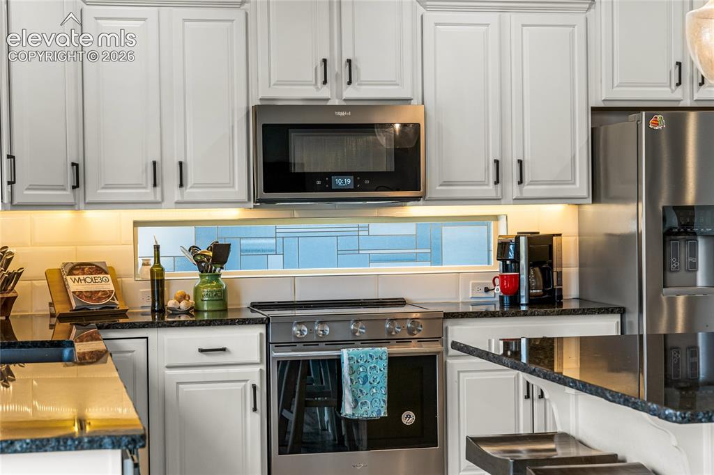 Image 4 of 32: Kitchen featuring a large island with dark countertops, white cabinetry, st
