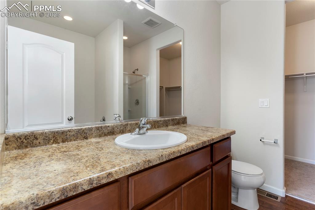 Image 24 of 35: Primary bath featuring a walk in closet, vanity, a stall shower, toilet, so