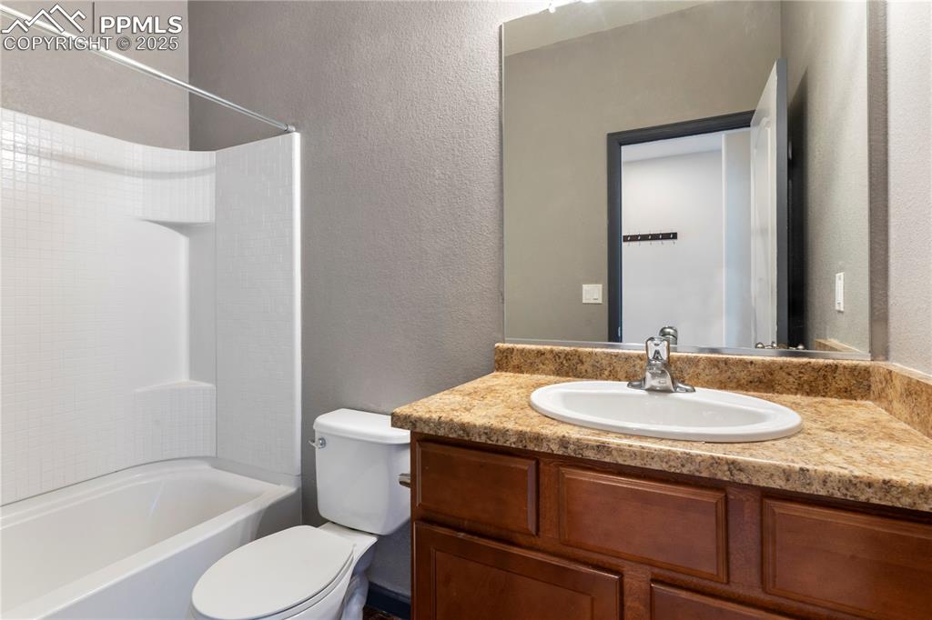 Image 7 of 35: Full bathroom featuring toilet, vanity, a textured wall, and tub / shower c