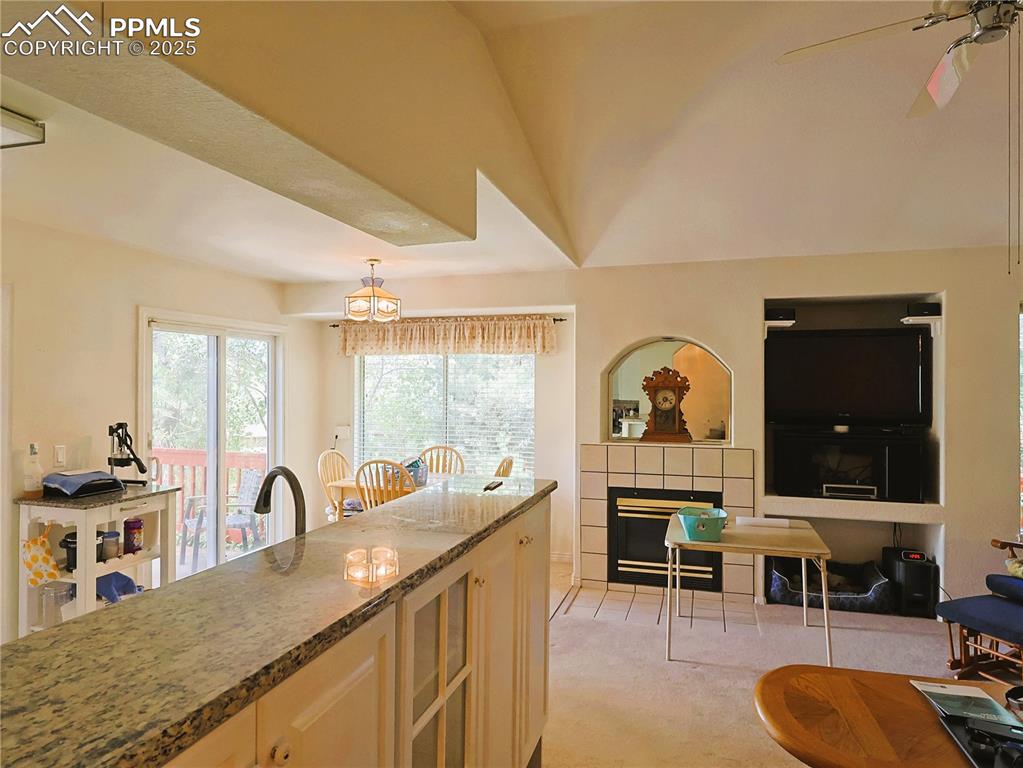 Image 10 of 29: Kitchen featuring dark stone counters, a tiled fireplace, ceiling fan, ligh