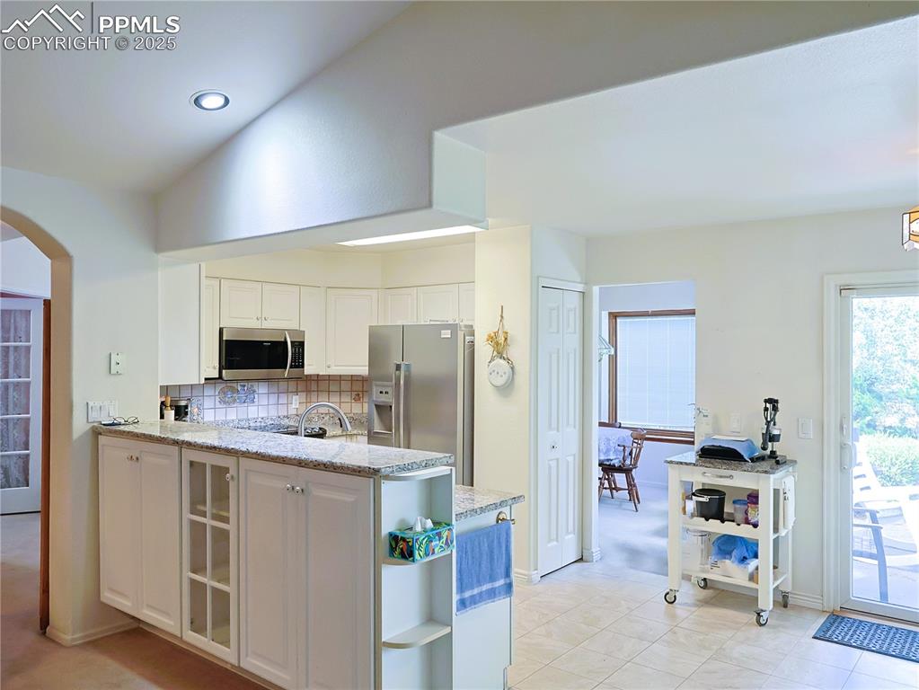 Image 8 of 29: Kitchen with a peninsula, open shelves, light stone countertops, backsplash