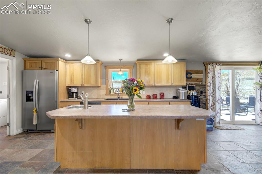 Image 12 of 50: Kitchen featuring light countertops, stainless steel fridge, an island with