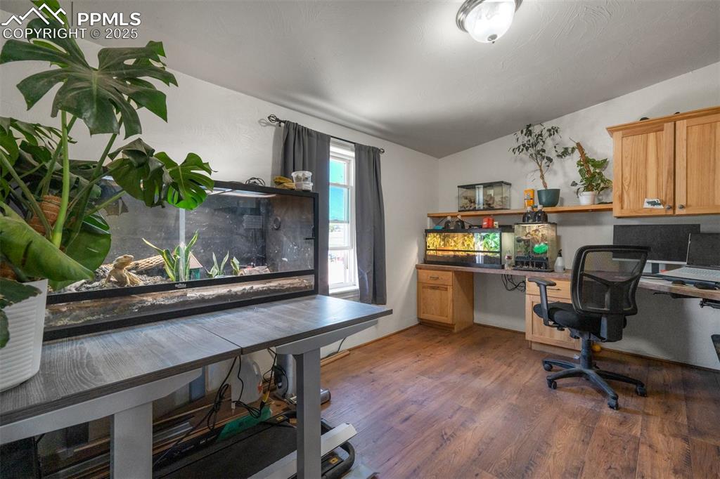 Image 20 of 50: Home office with built in study area, wood finished floors, and vaulted cei