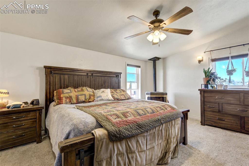 Image 22 of 50: Bedroom featuring multiple windows, light carpet, a wood stove, and ceiling