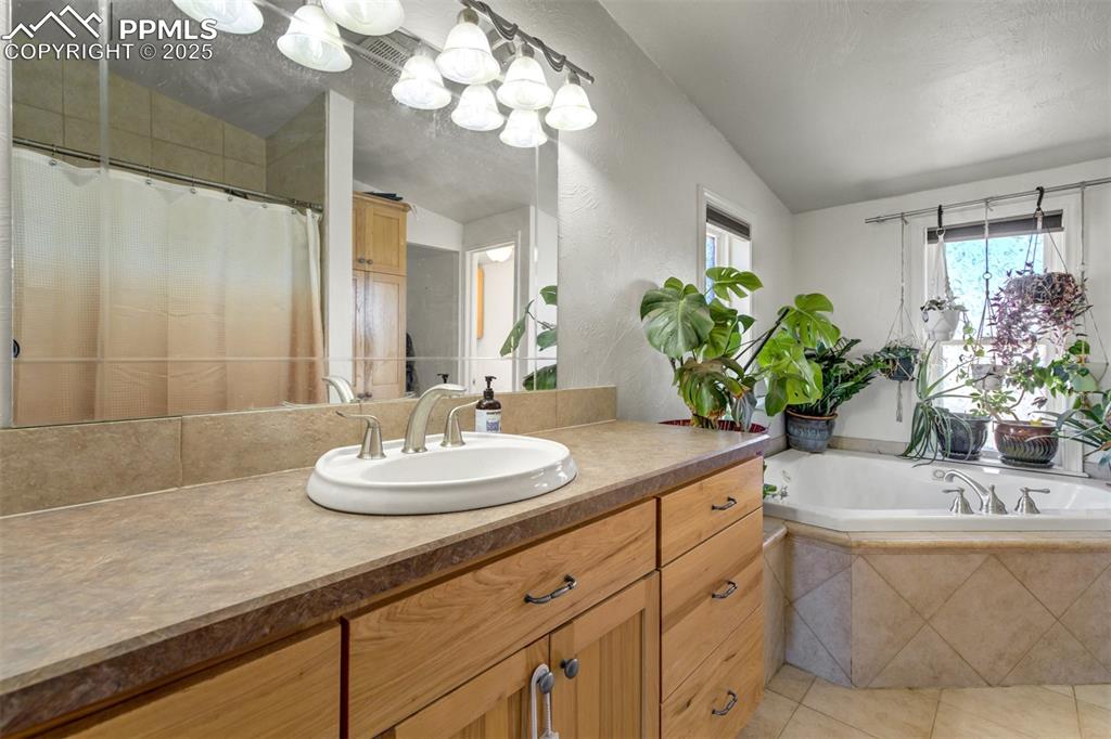 Image 25 of 50: Full bath featuring vanity, tile patterned floors, vaulted ceiling, and a h